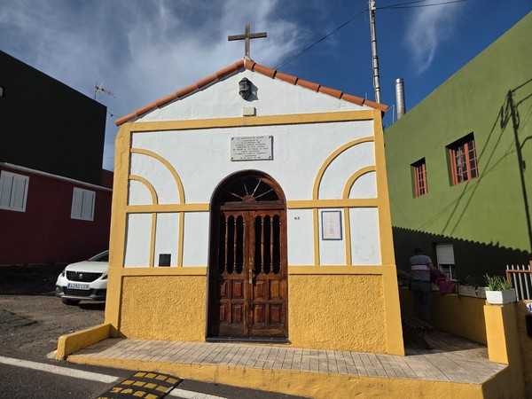 Façade blanche et ocre d’une petite chapelle à Aguamansa avec porte en bois et croix.