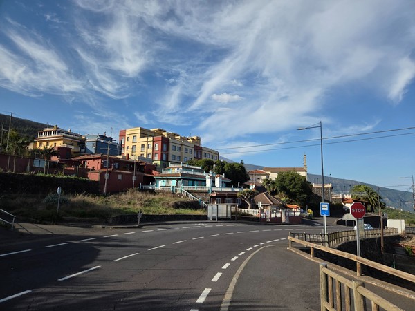 Courbe de la route d’accès à Aguamansa, avec des maisons colorées et le relief boisé en toile de fond.
