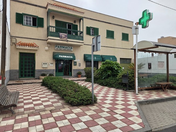 Bâtiment de la pharmacie de Villa de Arico avec croix verte lumineuse et auvent vert.