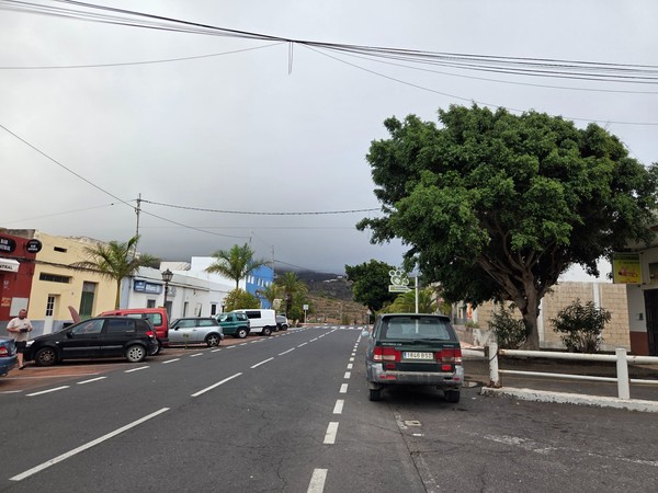 Vue d’ensemble de la rue principale de Villa de Arico, avec palmiers, façades basses et circulation légère sous un ciel nuageux.