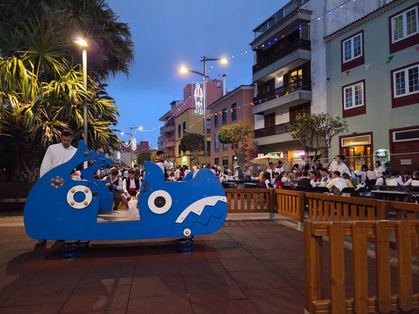Jeu pour enfants en forme de voiture bleue devant un square animé lors de la fête de La Laguna.