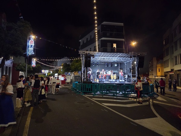 Groupe folklorique en concert sur une scène de rue avec percussions et chanteurs pendant la fête.
