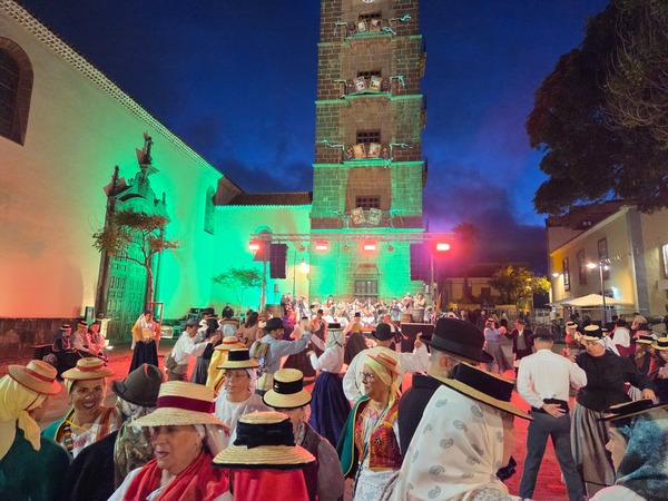 Couples en tenue traditionnelle canarienne dansant devant la tour de l’église de La Concepción éclairée.