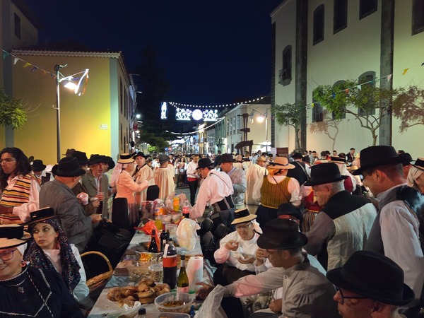 Place de la Concepción remplie de convives en costume, tour éclairée en rouge en arrière-plan.