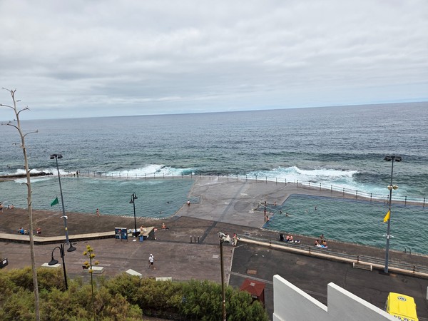 Grand bassin naturel de Bajamar avec des baigneurs et la houle de l’Atlantique derrière la barrière.