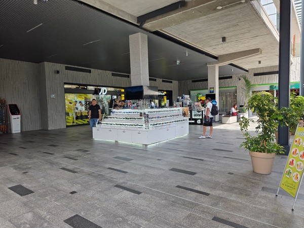 Allée couverte avec kiosque de lunettes au centre et boutiques autour, illustrant l’ambiance commerciale du Rosa Center.