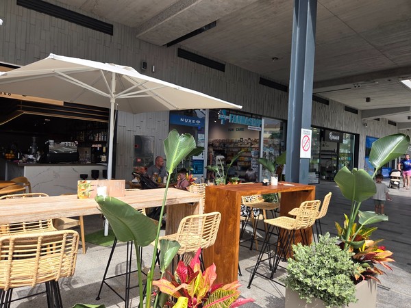 Espace café avec tables hautes, plantes et grand parasol, parfait pour une pause au Rosa Center.