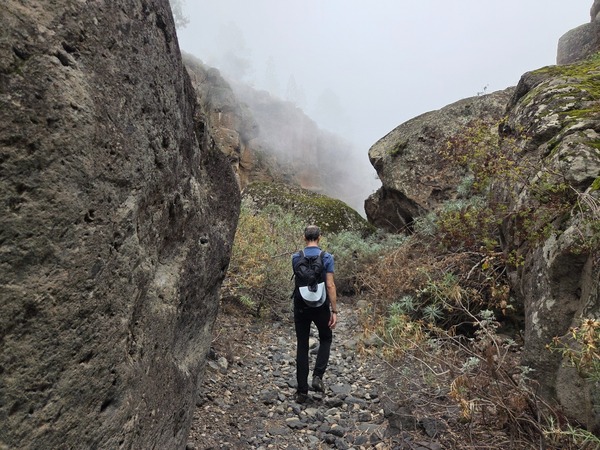 Passage étroit entre de grands blocs volcaniques dans un barranco couvert de brume.