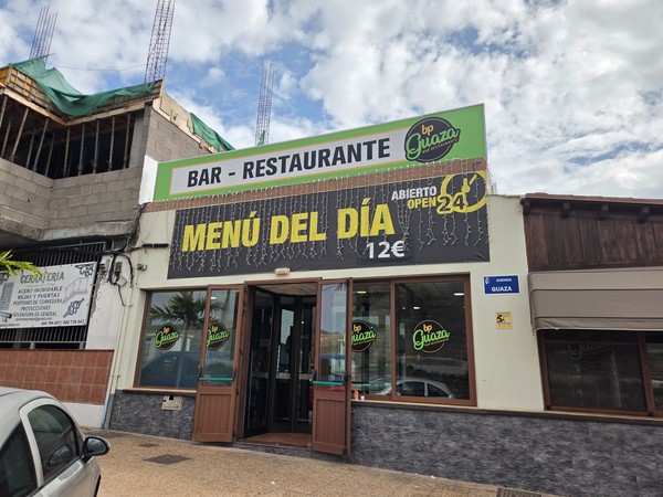 Façade du bar-restaurant bp Guaza à Tenerife avec une grande affiche annonçant un menu du jour à 12 euros et une ouverture 24 heures sur 24.