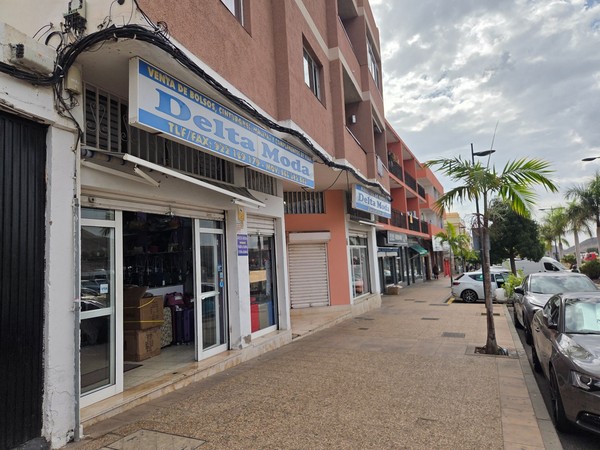 Rue commerciale de Guaza avec la boutique Delta Moda spécialisée dans la vente de sacs, ceintures et valises, bordée de palmiers et d’immeubles résidentiels.