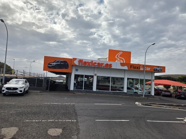 Bâtiment de l’agence de location de voitures Flexicar à Guaza avec une grande enseigne orange, des voitures exposées et un parking extérieur.
