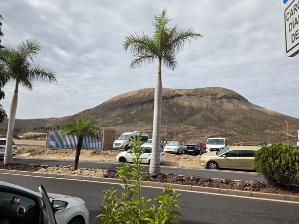 Vue de la montagne de Guaza à Tenerife avec des palmiers, des voitures garées et la route qui traverse ce paysage volcanique typique du sud de l’île.