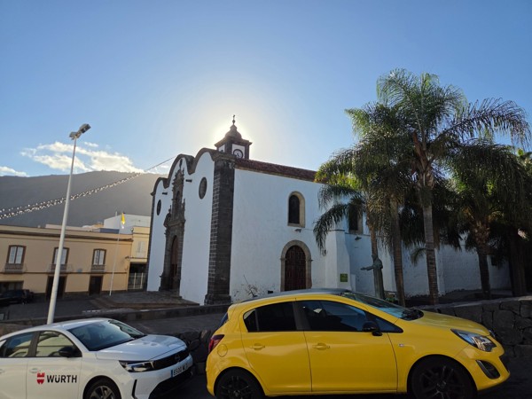 Vue latérale de l’église de San Pedro à Güímar avec des palmiers et la montagne au fond.