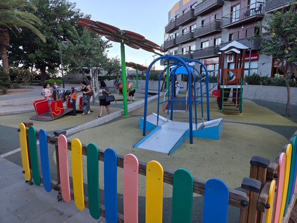 Aire de jeux pour enfants à Güímar avec balançoires, structure colorée et familles profitant du parc.