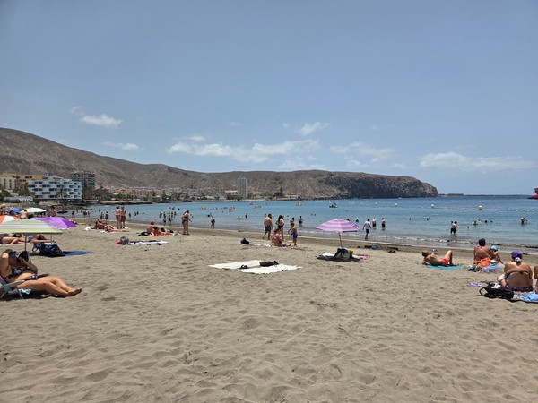 Baignade et bronzage sur la plage animée de Los Cristianos entourée de collines volcaniques.