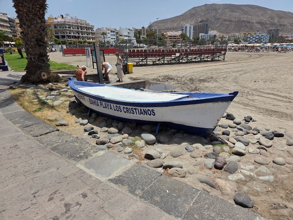 Ancienne barque peinte en blanc et bleu portant le nom Bahia Playa Los Cristianos près de la plage.