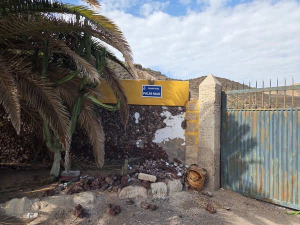 Ancien mur en pierre volcanique avec un panneau de rue Carretera Palm-Mar, un grand cactus et un portail métallique rouillé à l’entrée d’un chemin.