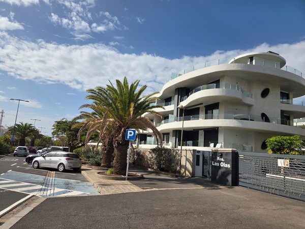 Résidence Las Olas à Palm-Mar avec façades blanches arrondies, grandes terrasses vitrées et palmiers le long de la rue.