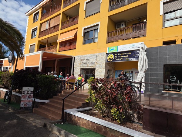 Immeuble ocre à Palm-Mar avec terrasse de café animée, salon de beauté et bureau d’assurance All Properties & All Insurance Tenerife.