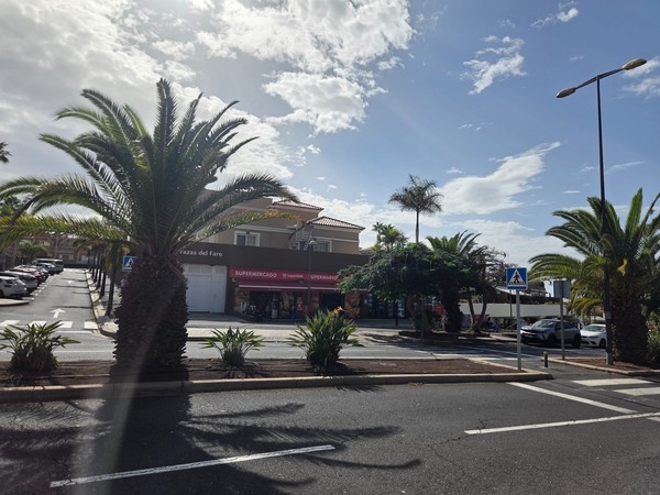 Bâtiment du supermarché de quartier à Palm-Mar, entouré de palmiers et de places de parking, sous un ciel lumineux.