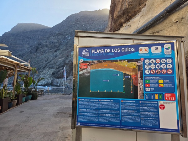 Mur d’entrée avec l’inscription « Playa de Los Guíos » et des formes géométriques adossé à la roche.