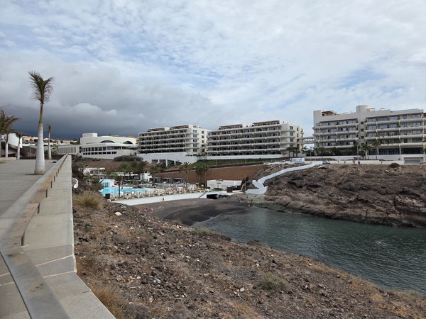 Vue lointaine de Playa El Pinque montrant la crique noire, la jetée et les résidences en terrasses au-dessus de la plage.