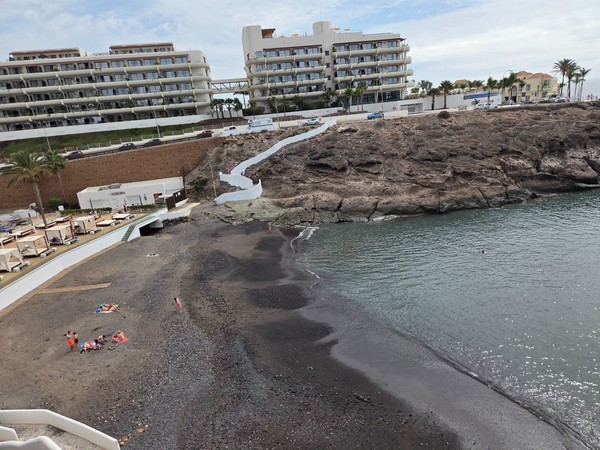Panorama sur Playa El Pinque depuis la promenade : escaliers blancs, anse abritée et ligne de palmiers le long des hôtels.