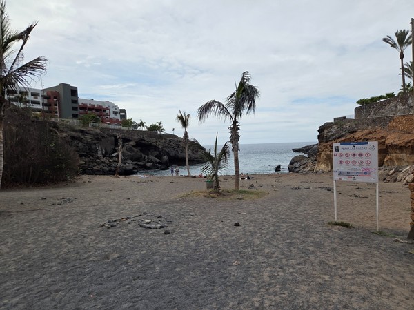 Panneau d'accès Playa Las Galgas avec pictogrammes et sable noir à l'entrée de la plage.