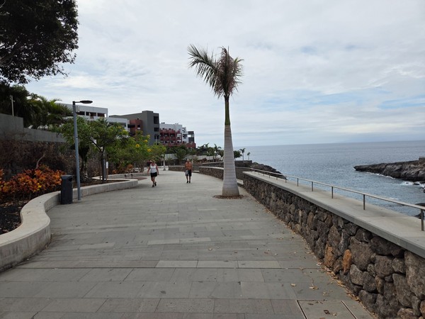 Promenade piétonne moderne bordant la côte près de Playa Las Galgas avec muret en pierre et mer calme.