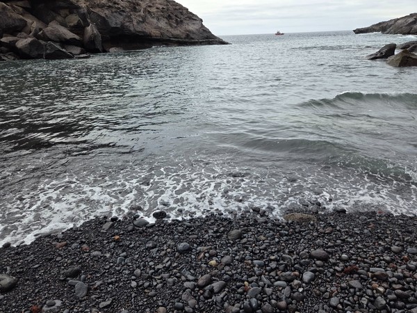 Bord de mer à Playa Las Galgas avec galets volcaniques sombres et vagues douces.