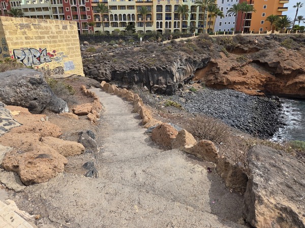 Sentier piéton sécurisé longeant la falaise vers Playa Las Salinas, bordé de pierres volcaniques.