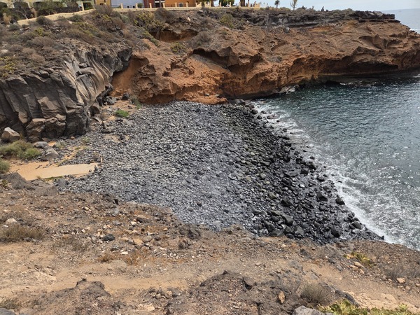 Vue plongeante sur la plage de galets noirs de Playa Las Salinas avec la mer calme et les falaises de lave.