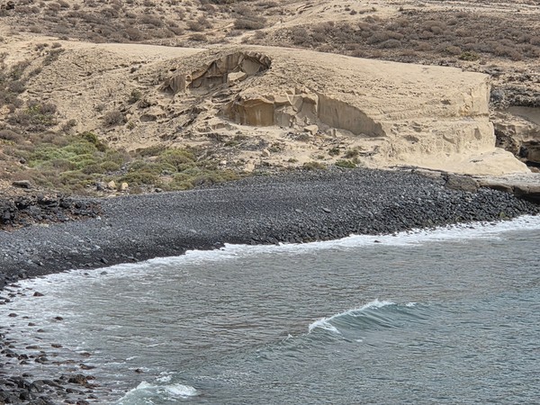 Gros plan sur la falaise claire au-dessus de la grève sombre de Playa Pardela, avec des formes taillées par le vent et la mer.