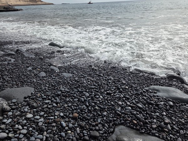 Galets noirs brillants au contact de l’écume, texture serrée et reflets à Playa Pardela.